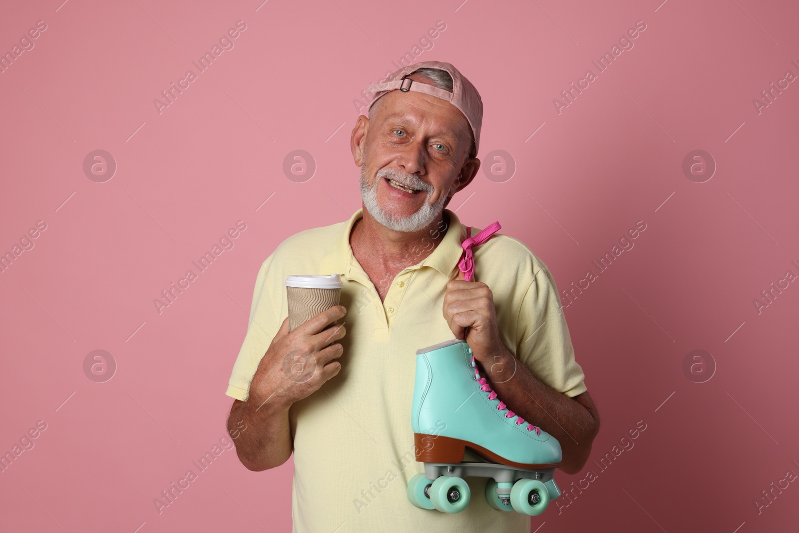 Photo of Portrait of happy senior man with paper cup and roller skates on pink background