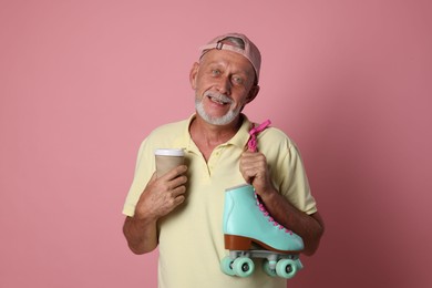 Photo of Portrait of happy senior man with paper cup and roller skates on pink background