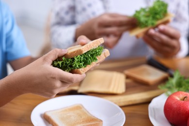 Photo of Boy and his mother preparing lunch box with healthy snacks at wooden table in kitchen, closeup