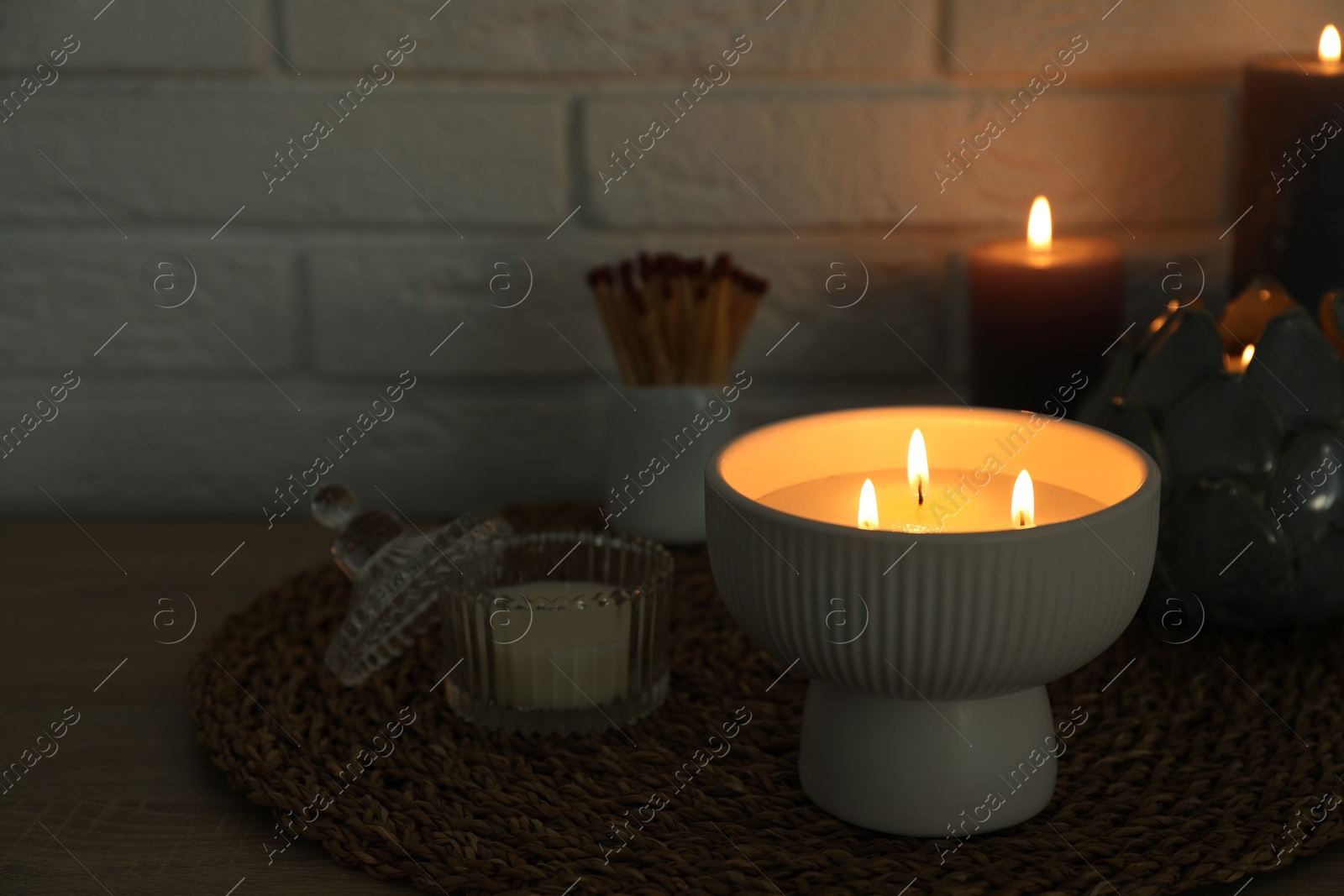 Photo of Burning candles and decor on table near white brick wall. Space for text