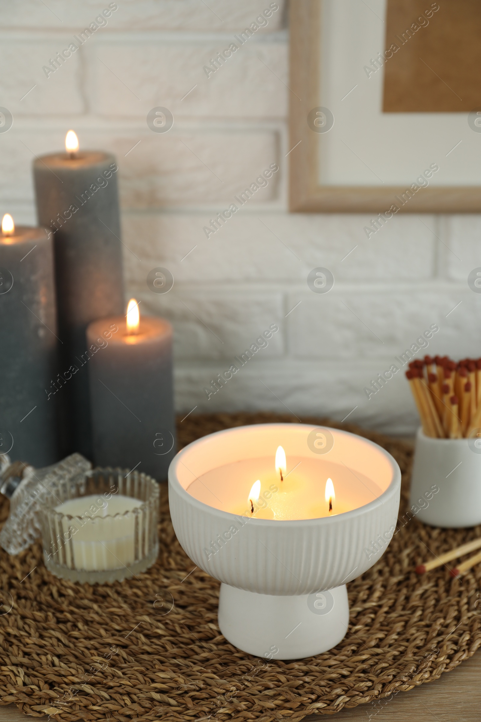 Photo of Burning candles and decor on table near white brick wall