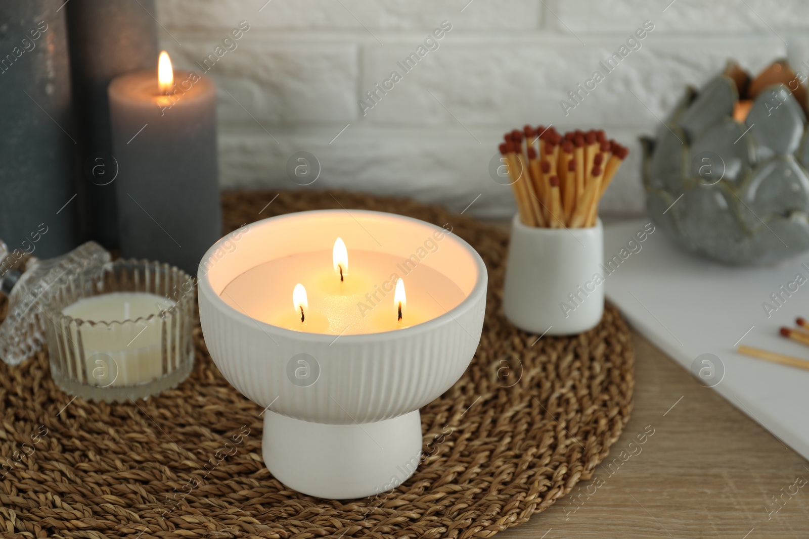 Photo of Burning candles and decor on table near white brick wall