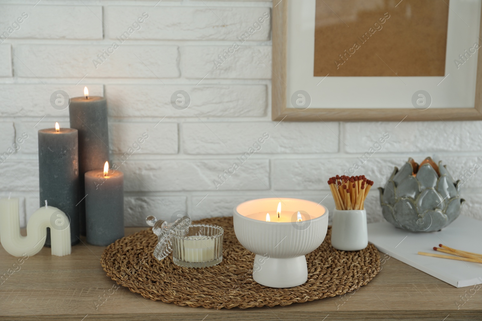 Photo of Burning candles and decor on table near white brick wall