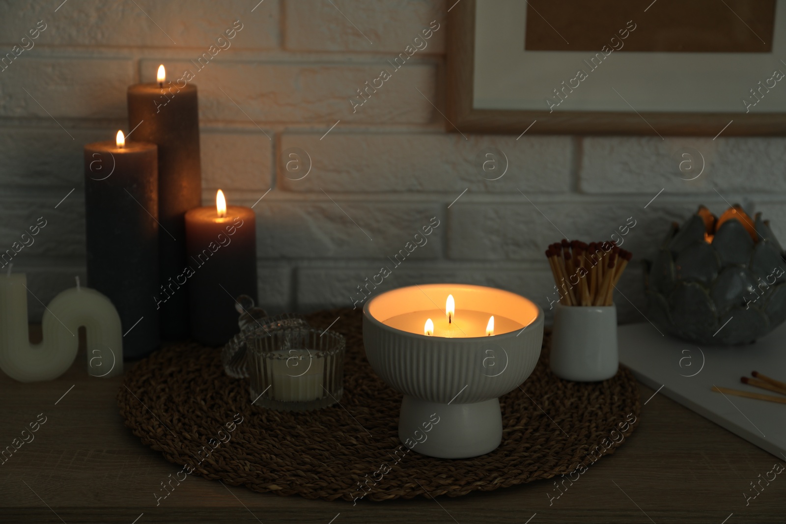 Photo of Burning candles and decor on table near white brick wall