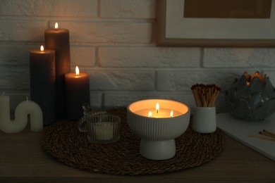 Photo of Burning candles and decor on table near white brick wall