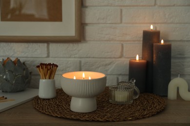 Photo of Burning candles and decor on table near white brick wall