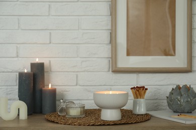 Photo of Burning candles and decor on table near white brick wall