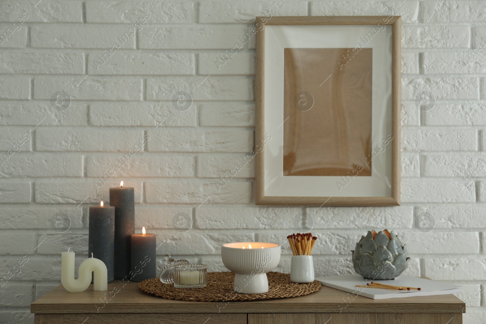 Photo of Burning candles and decor on table near white brick wall