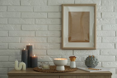 Burning candles and decor on table near white brick wall