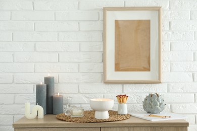 Photo of Burning candles and decor on table near white brick wall