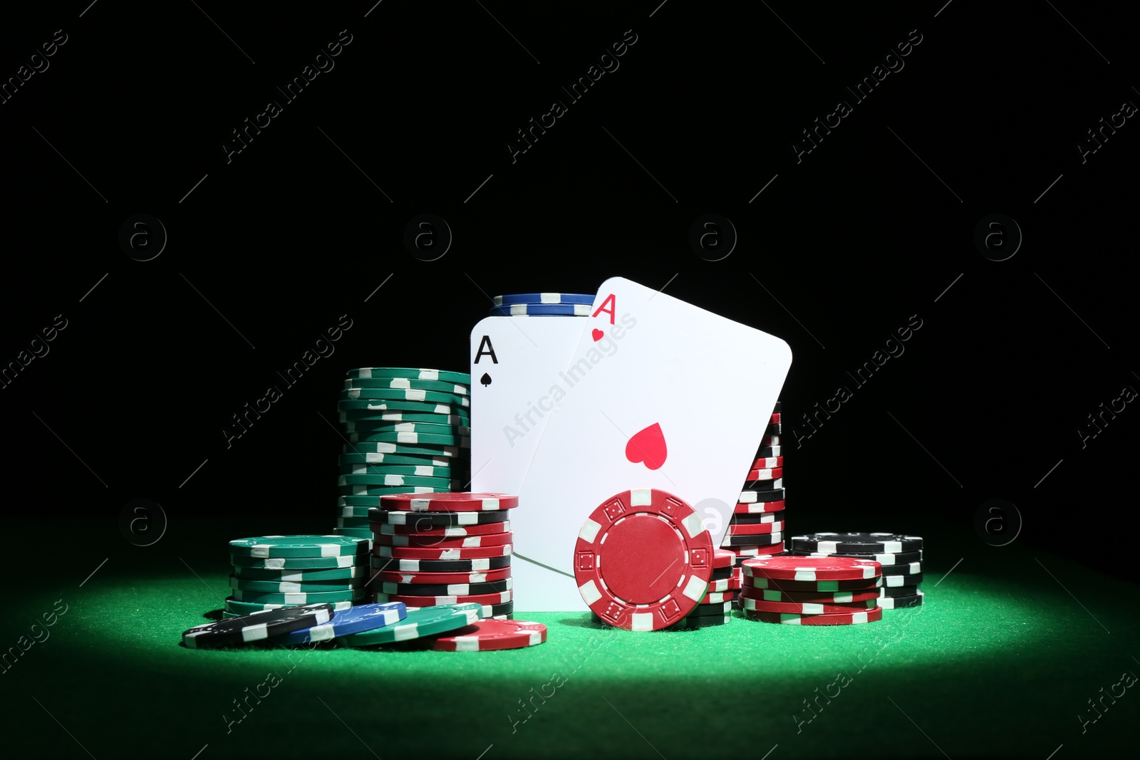 Photo of Playing cards and poker chips on green table against dark background