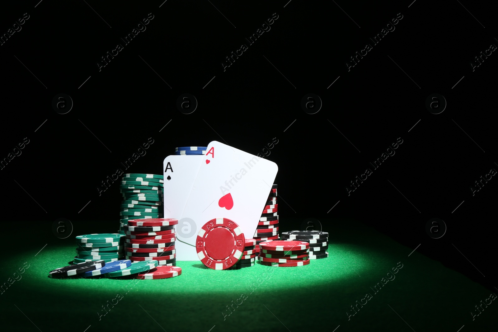 Photo of Playing cards and poker chips on green table against dark background