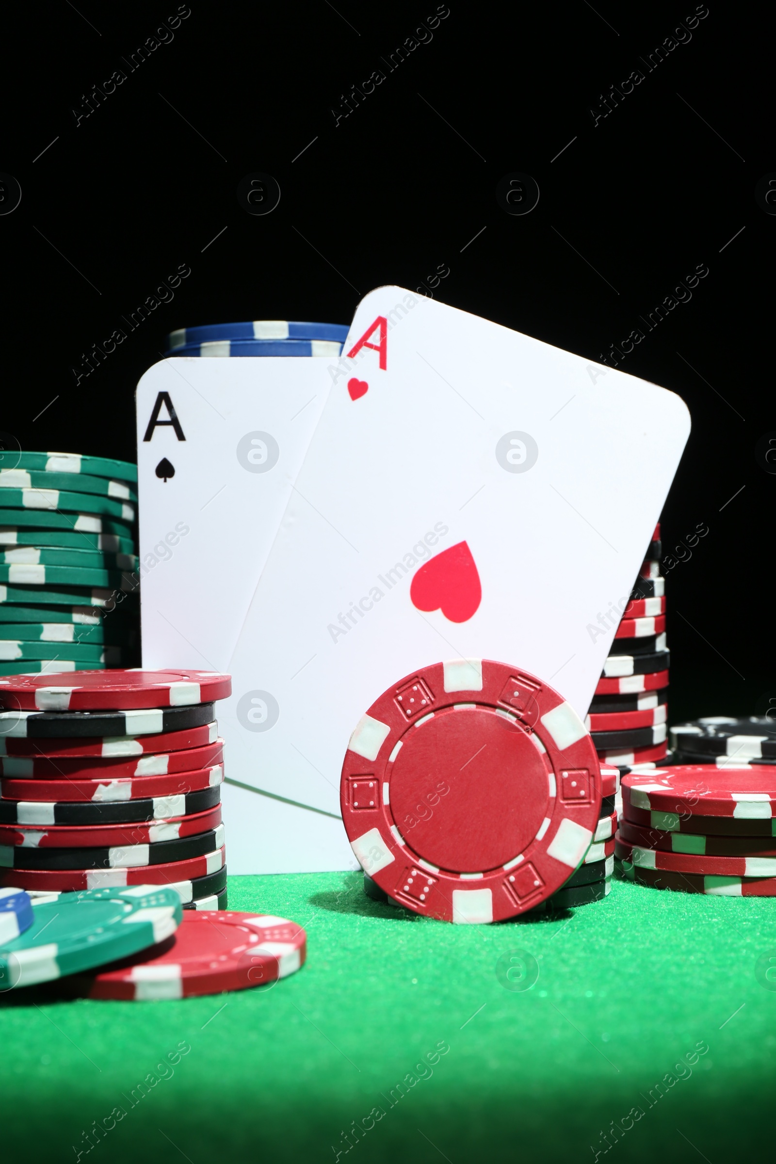 Photo of Playing cards and poker chips on green table against dark background