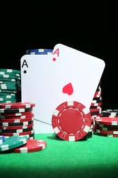 Photo of Playing cards and poker chips on green table against dark background