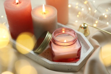 Beautiful burning candles on fabric against blurred lights