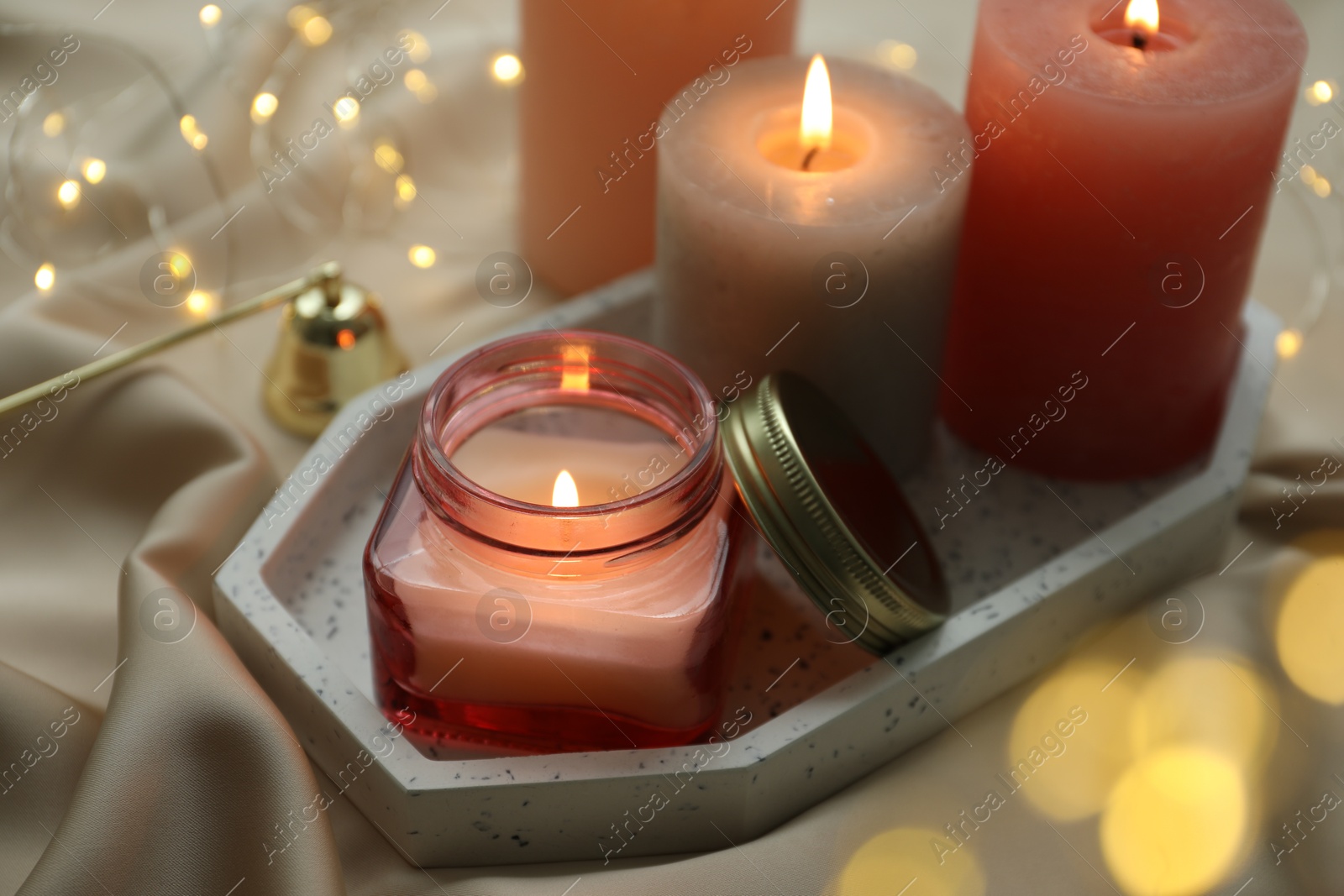 Photo of Beautiful burning candles on fabric against blurred lights