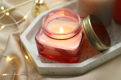 Beautiful burning candles on fabric against blurred lights, closeup