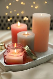 Photo of Beautiful burning candles on fabric against blurred lights, closeup