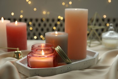 Beautiful burning candles on fabric against blurred lights