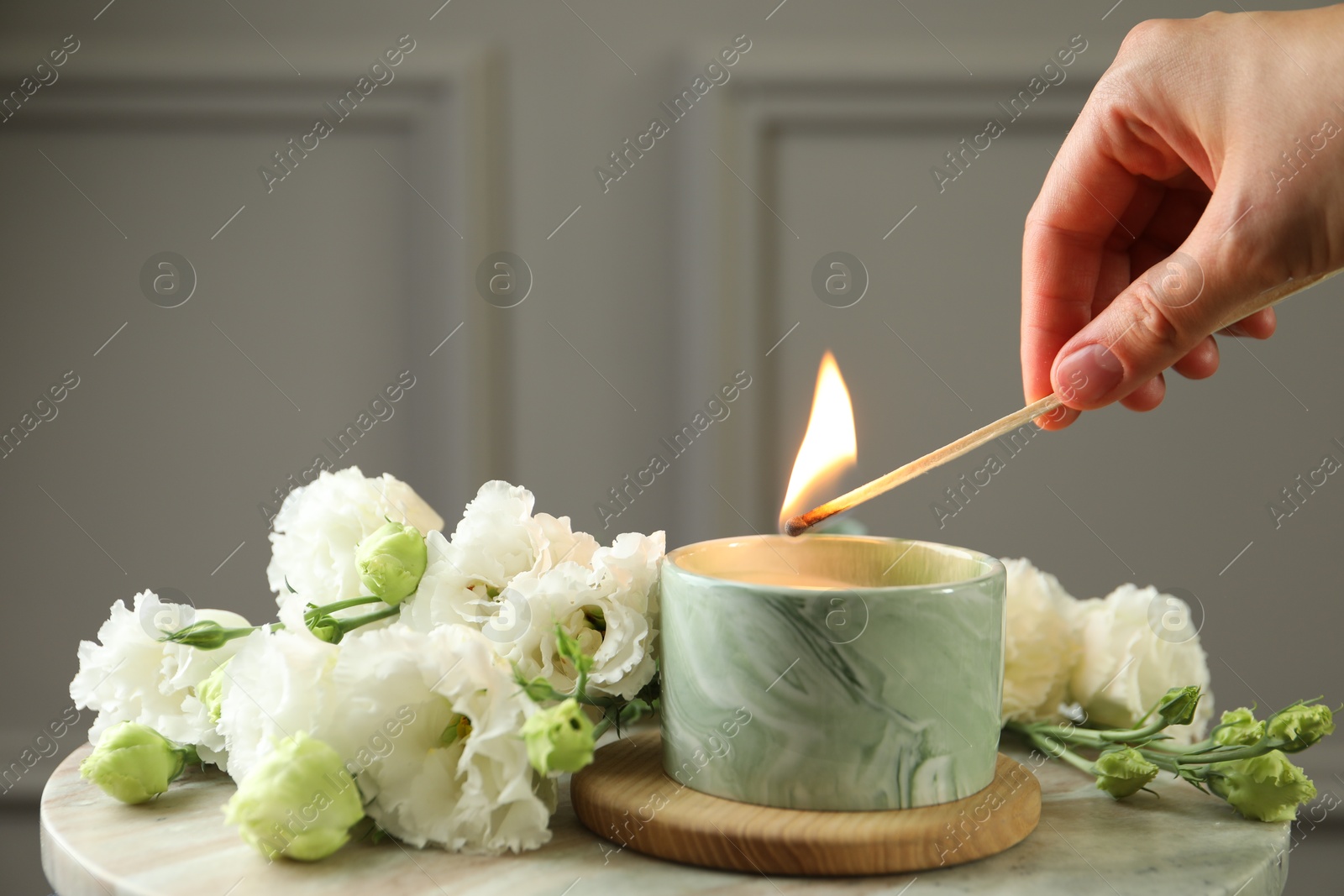 Photo of Woman lighting candle at table with beautiful flowers, closeup