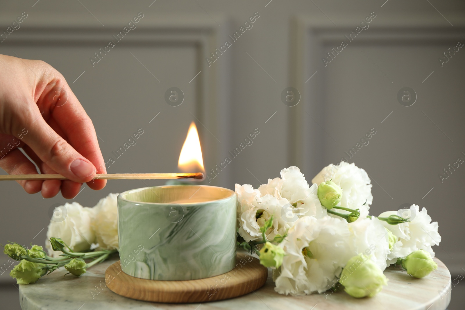 Photo of Woman lighting candle at table with beautiful flowers, closeup