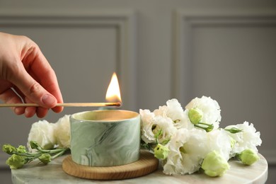 Woman lighting candle at table with beautiful flowers, closeup