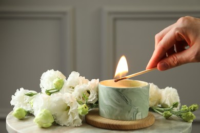 Photo of Woman lighting candle at table with beautiful flowers, closeup