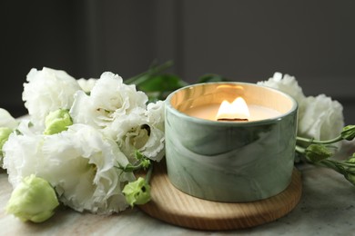 Photo of Burning candle and beautiful flowers on marble table, closeup