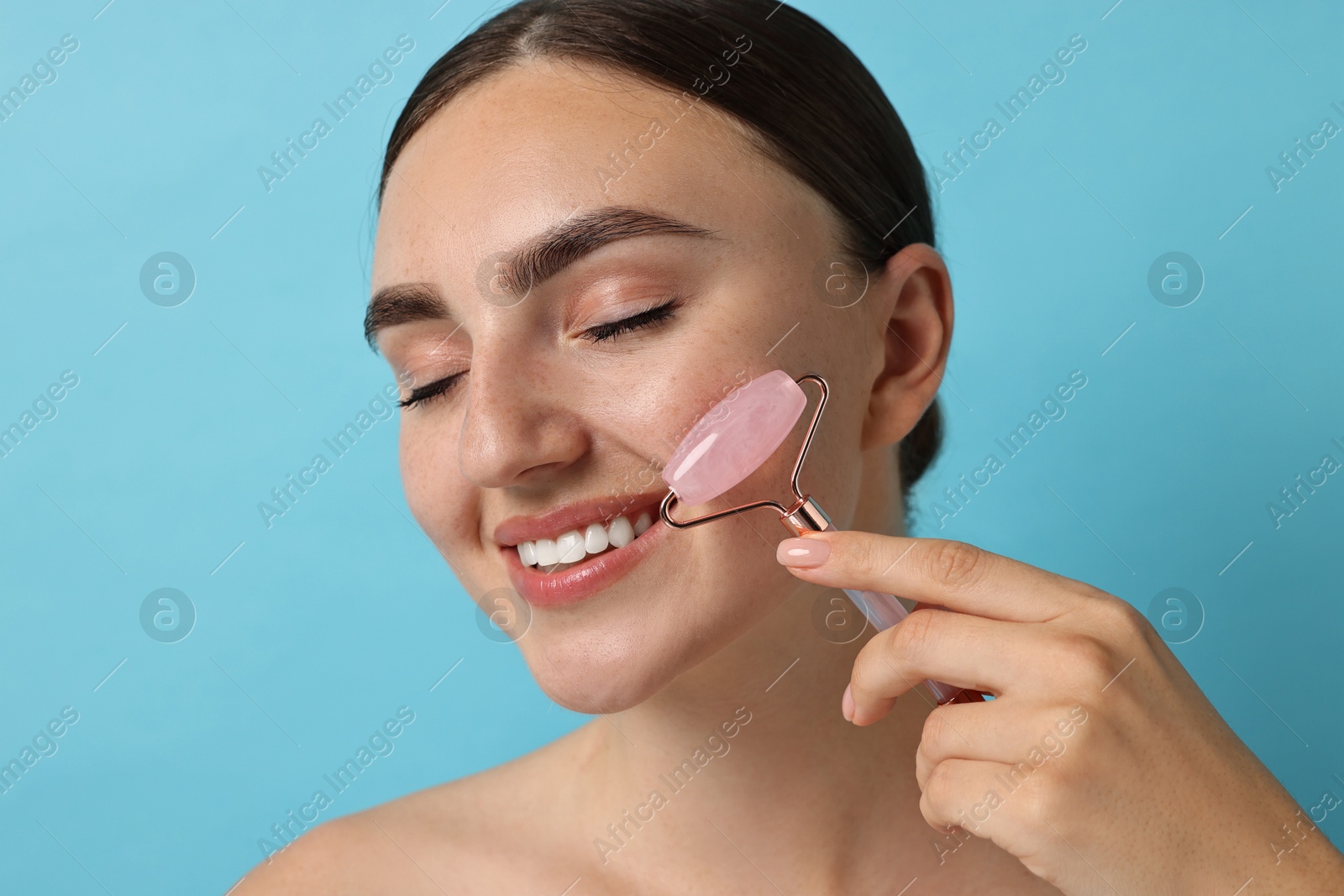 Photo of Beautiful young woman doing facial massage with roller on light blue background