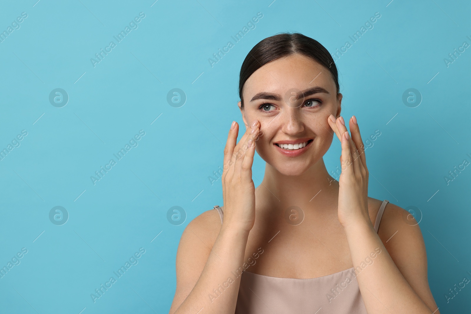 Photo of Face massage. Beautiful young woman with healthy skin on light blue background, space for text