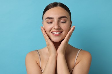 Beautiful young woman with healthy skin on light blue background