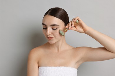 Photo of Beautiful young woman doing facial massage with roller on grey background