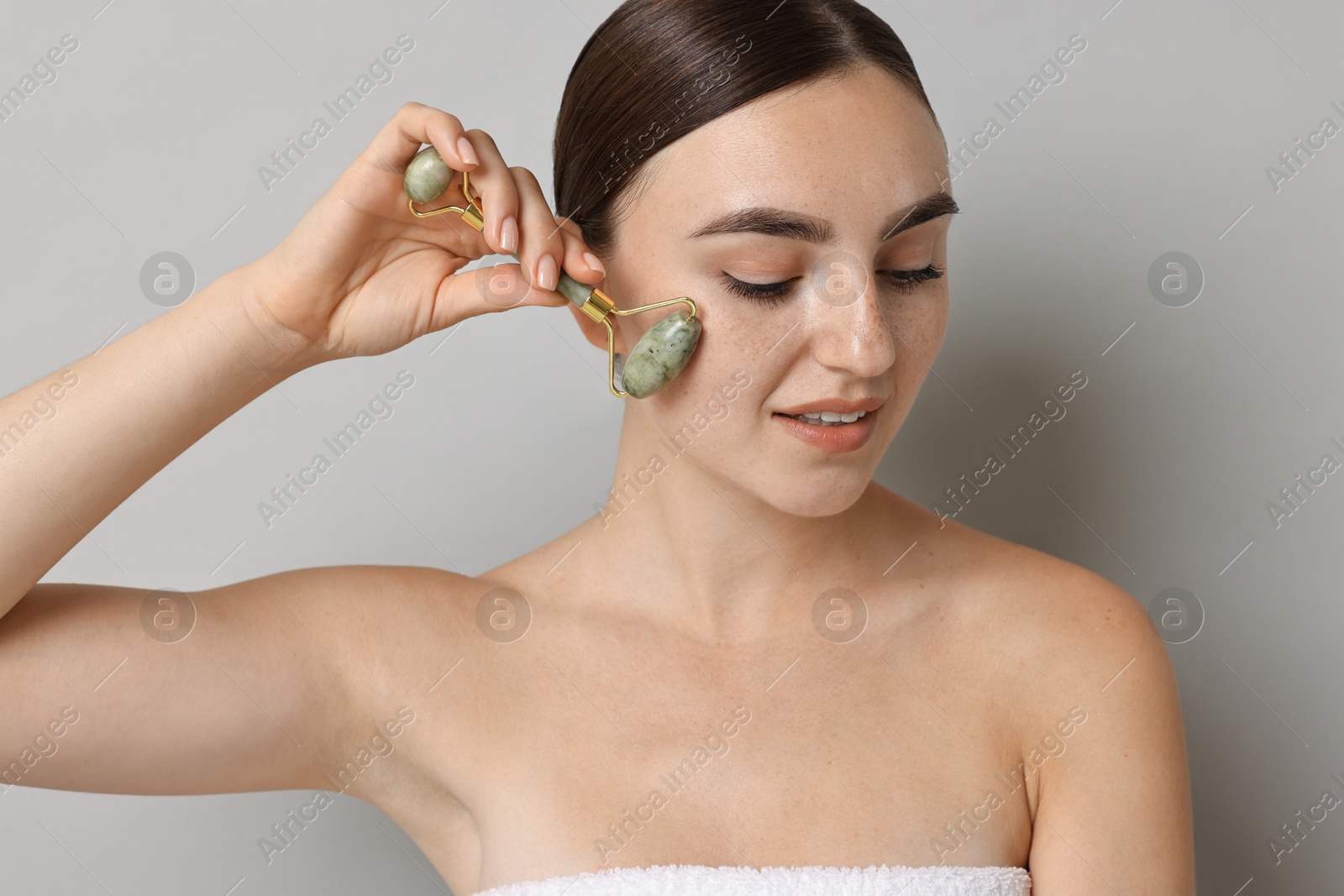 Photo of Beautiful young woman doing facial massage with roller on grey background