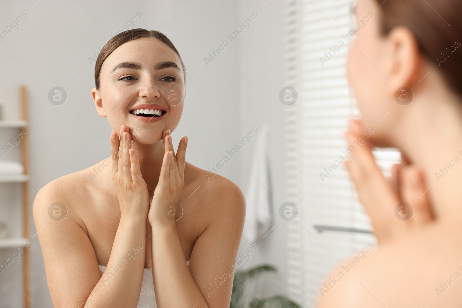 Photo of Face massage. Beautiful young woman with healthy skin near mirror at home