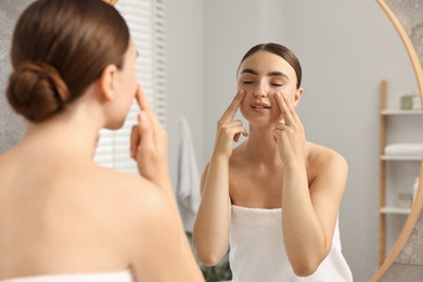 Beautiful young woman doing facial massage near mirror at home