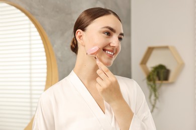 Photo of Beautiful young woman doing facial massage with roller at home