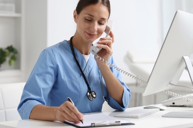 Nurse consulting patient by phone at white table in clinic