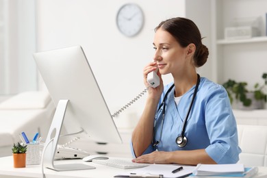 Photo of Nurse consulting patient by phone at white table in clinic