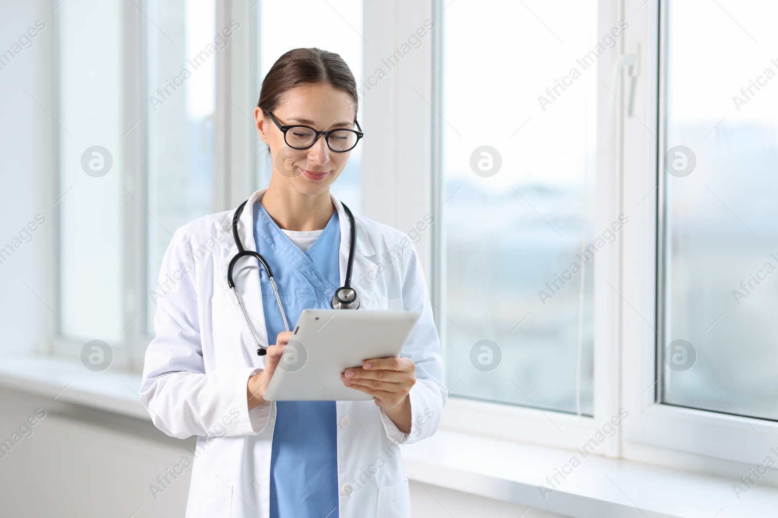 Photo of Nurse with stethoscope using tablet near window in clinic