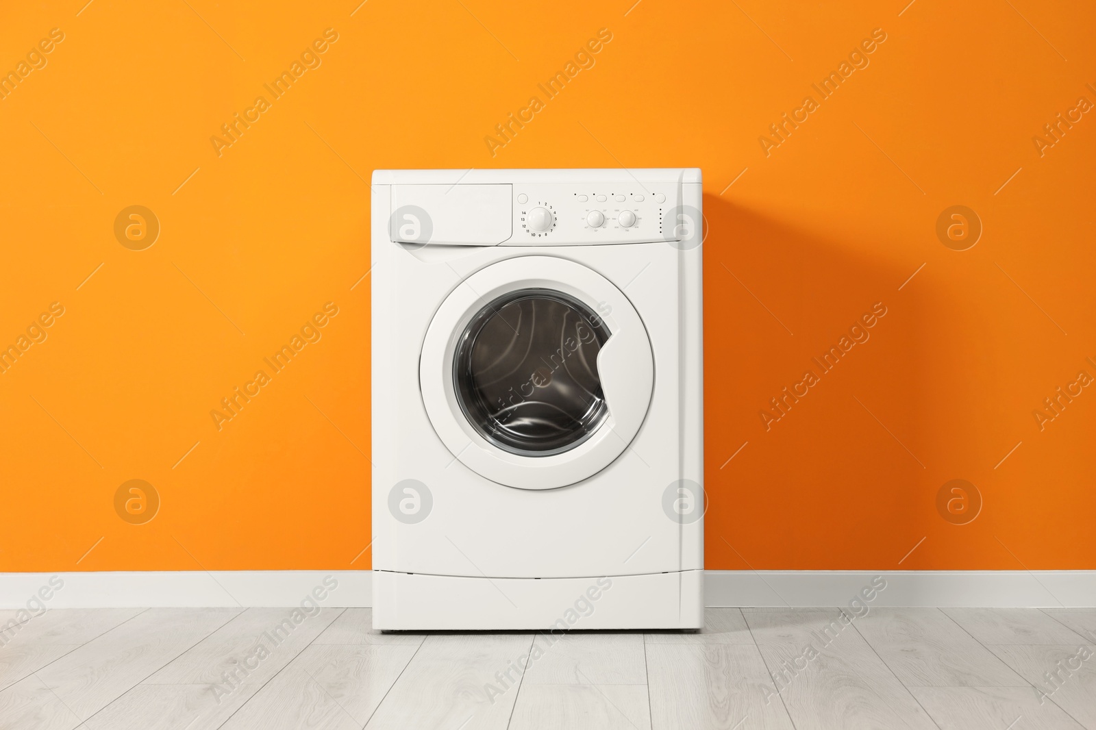 Photo of One washing machine near orange wall indoors