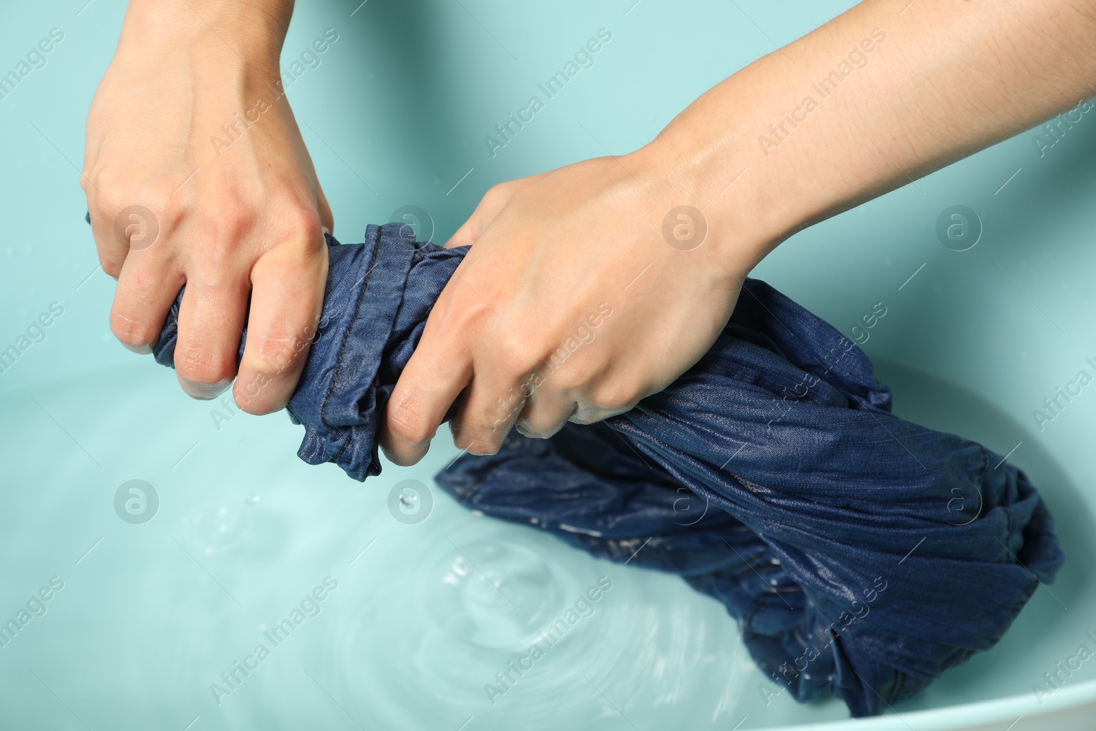 Photo of Woman washing denim clothes in basin, closeup