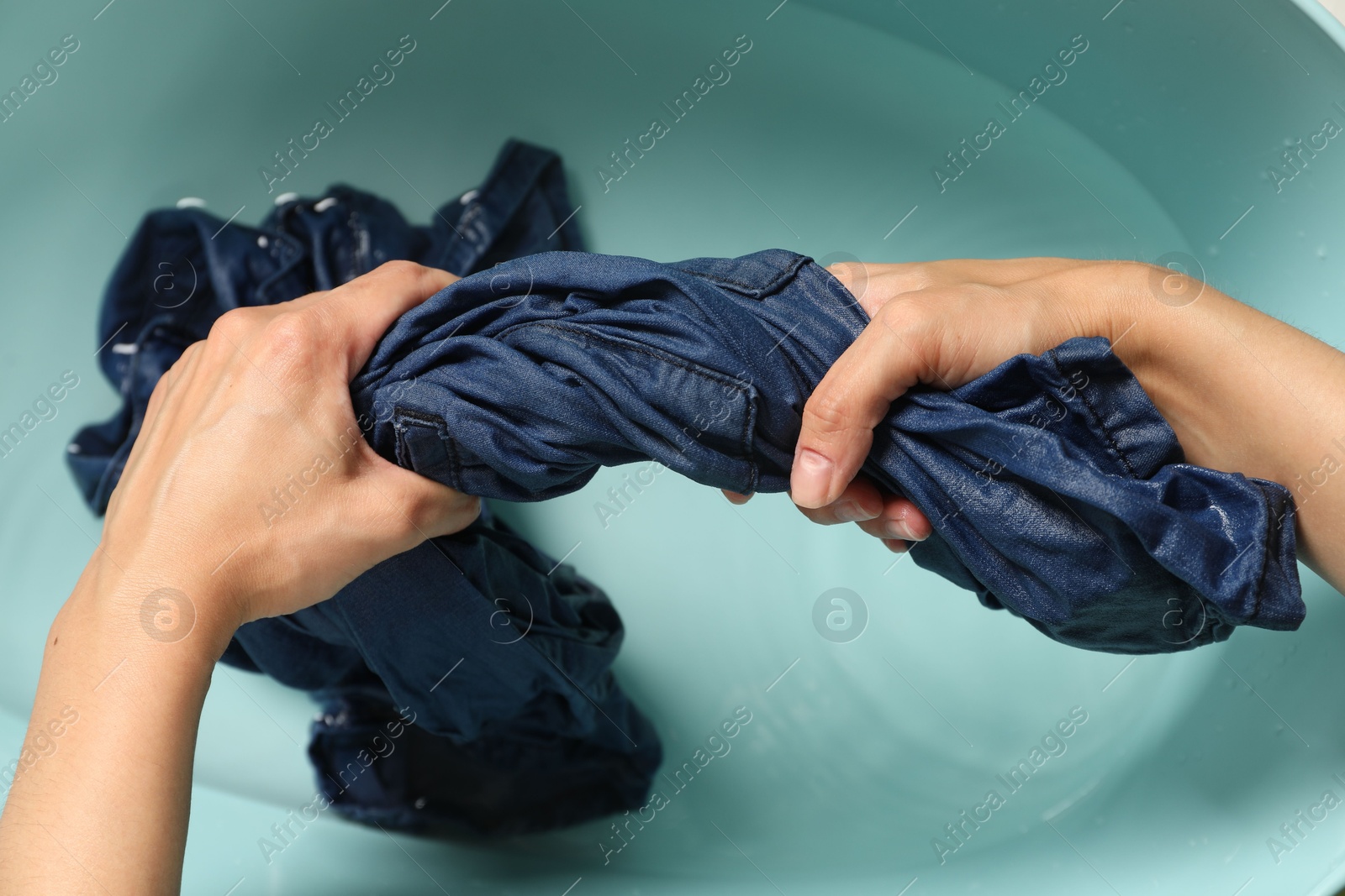 Photo of Woman washing denim clothes in basin, top view