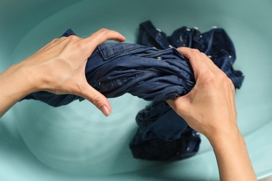 Photo of Woman washing denim clothes in basin, top view