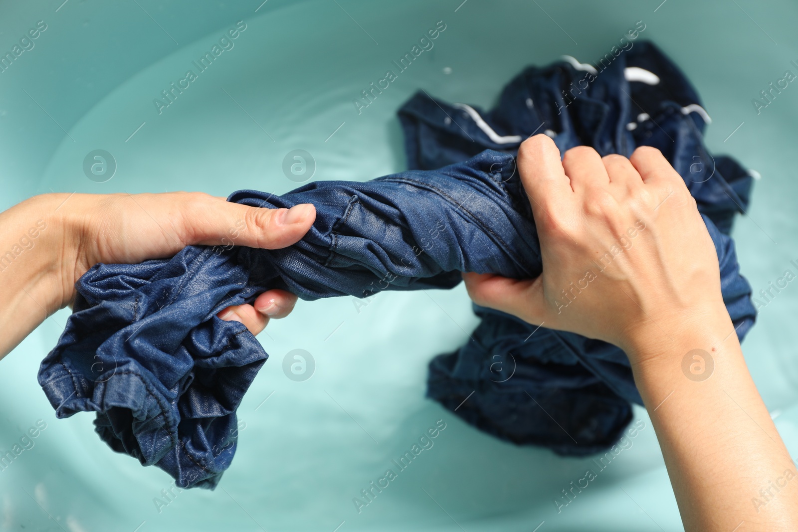 Photo of Woman washing denim clothes in basin, top view