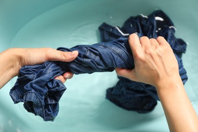 Woman washing denim clothes in basin, top view