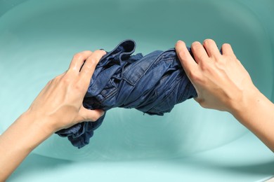 Photo of Woman washing denim clothes in basin, top view