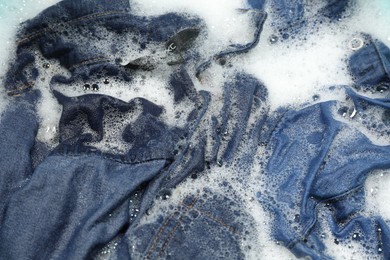 Photo of Many different denim clothes in basin with water and soap, top view