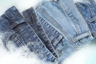 Photo of Many different denim clothes in basin with water and soap, top view