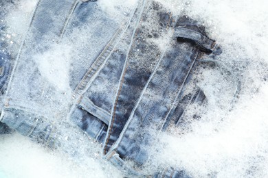 Photo of Many different denim clothes in basin with water and soap, top view