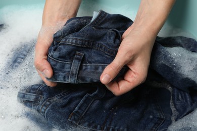 Photo of Woman washing denim clothes with soap and water in basin, closeup